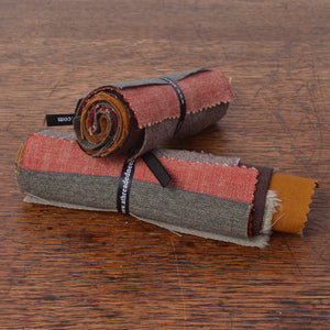 Two rolled fabric swatches with visible woven texture . The fabrics show muted red, grey, brown, mustard yellow, and green tones.