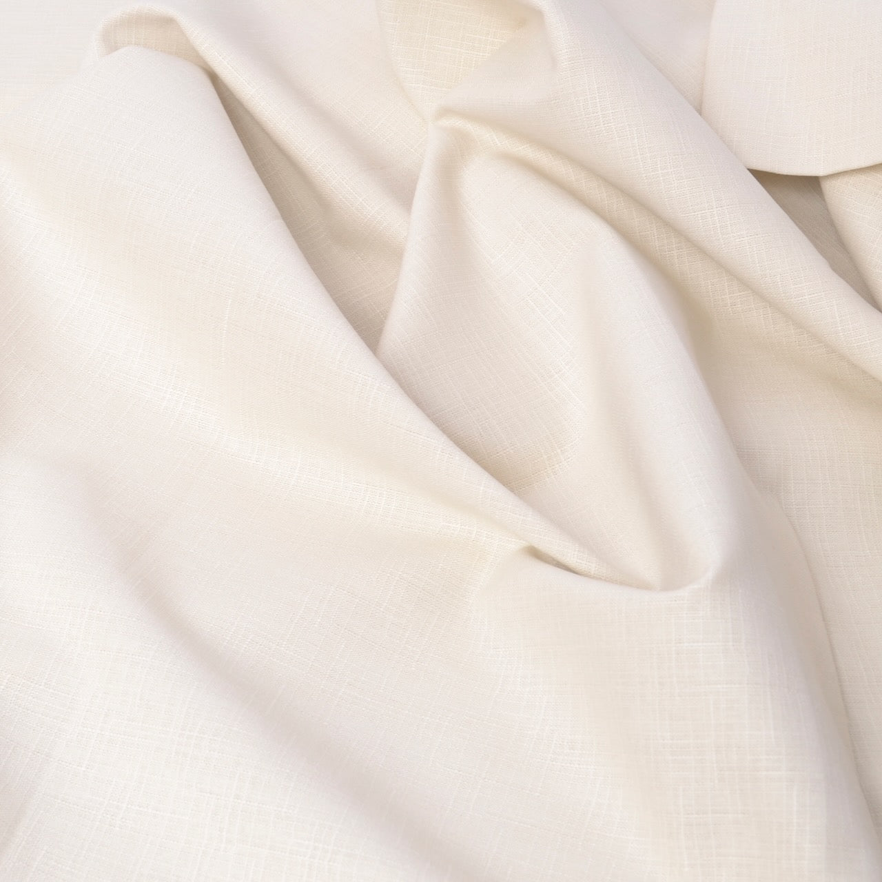 A close-up of draped off-white fabric with a subtle woven texture, showing soft folds and shadows.
