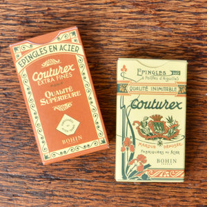 Two vintage Bohin Couturex boxes for sewing pins displayed side-by-side on a dark wood background. 