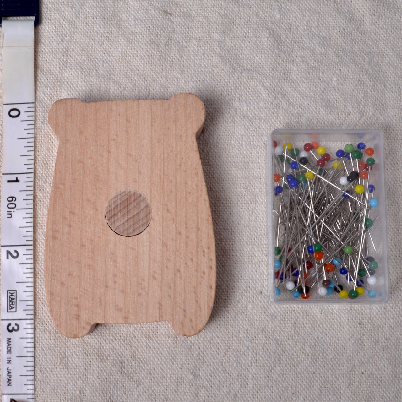 Wooden bear-shaped pin cushion with a container of pins on a textured fabric background