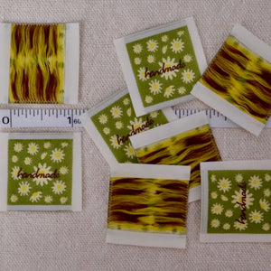 one inch cloth labels with text reading "handmade" bright green with daisies