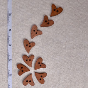Wooden heart-shaped buttons on a beige fabric background with a ruler for scale.