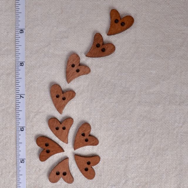Wooden heart-shaped buttons on a beige fabric background with a ruler for scale.