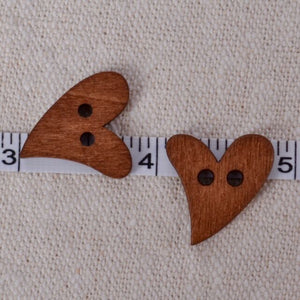 Two wooden heart-shaped buttons with a measuring tape showing their size on a textured beige background.