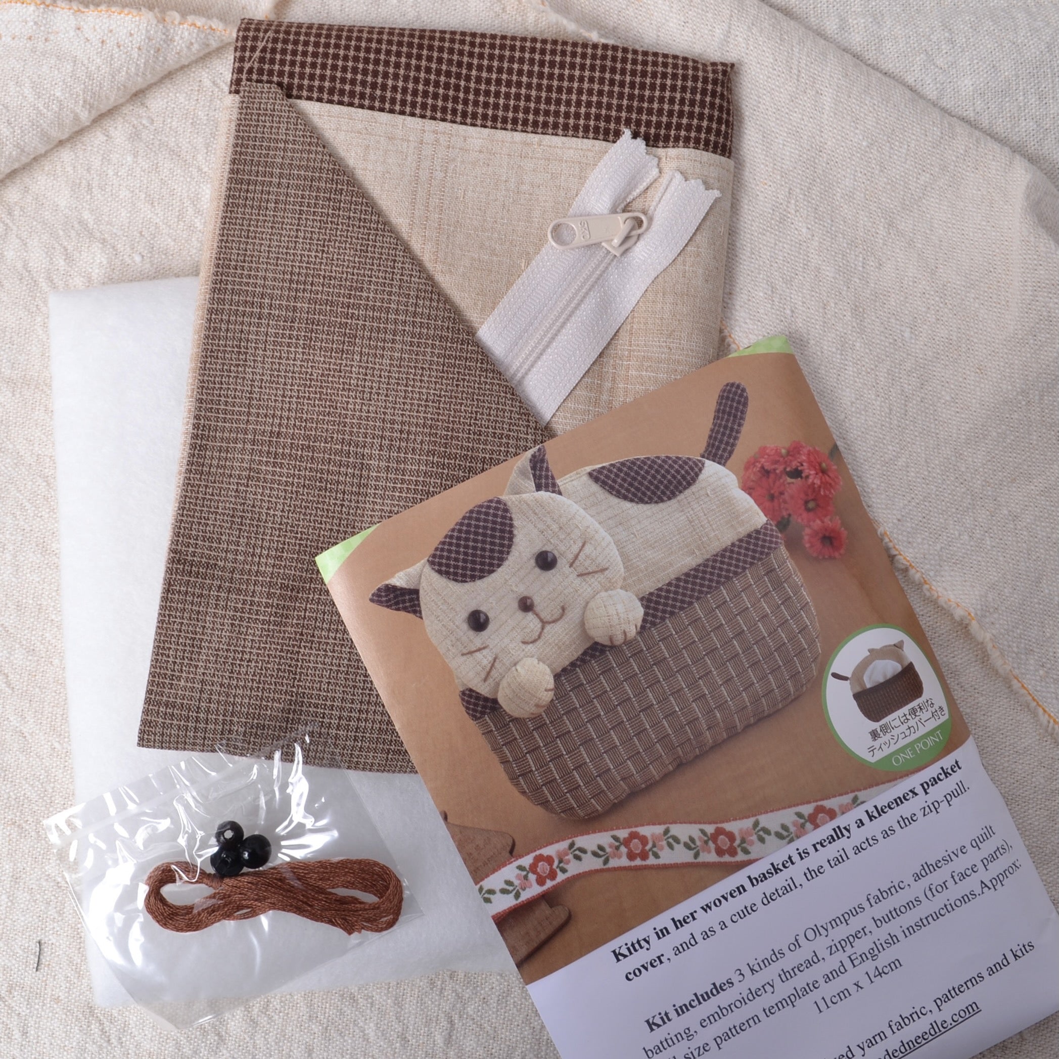 A kit to create a tissue cover with a cute kitten design, including cotton fabrics, iron-on quilt batting, zipper, embroidery threads, and a pattern piece.