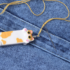 showing step 2 for how to use needle threader by puling the needle up over the thread, spotted yellow kitten