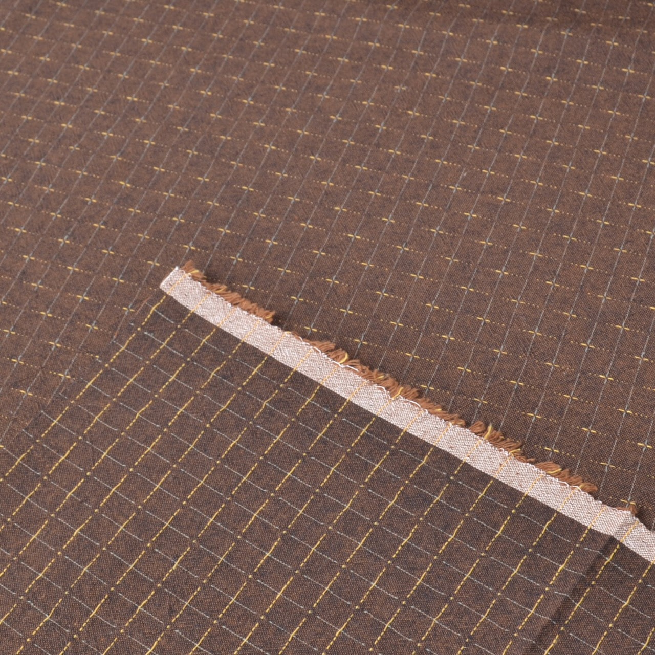 A close-up of a dark brown woven fabric with a fine grid pattern showing both sides of the fabric and the salvage