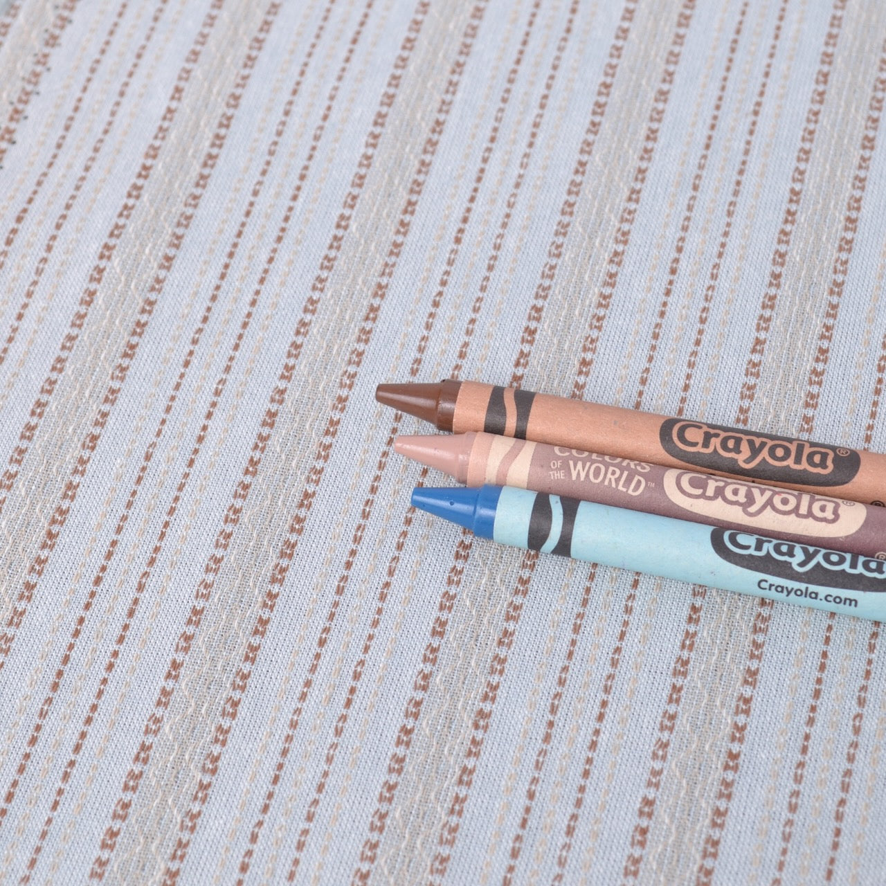 Three Crayola crayons on dyed yarn cotton fabric to show colours