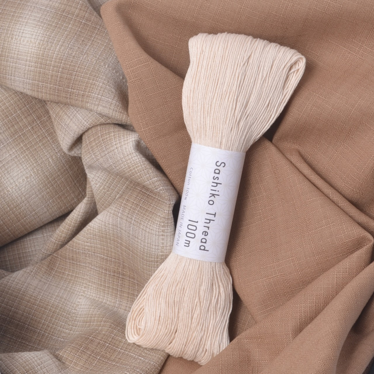 A skein of cream-colored Sashiko thread resting on draped beige fabric. 