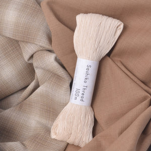 A skein of cream-colored Sashiko thread resting on draped beige fabric. 