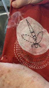 video showing dissolvable peel and stick being washed away from finished dragonfly stitching